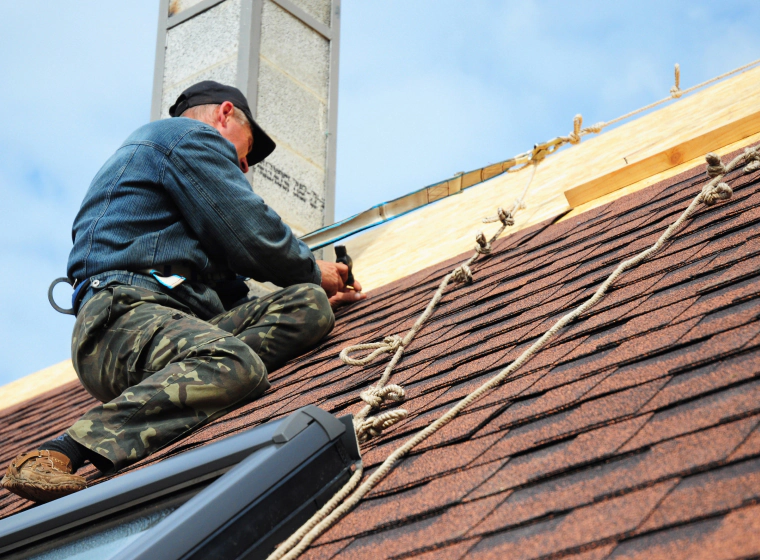 man with harness installing shingles on the roof